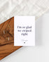 A white postcard laying on a wooden board with some golden triangle paperclips and a white cloth in the background. The postcard design reads "I&
