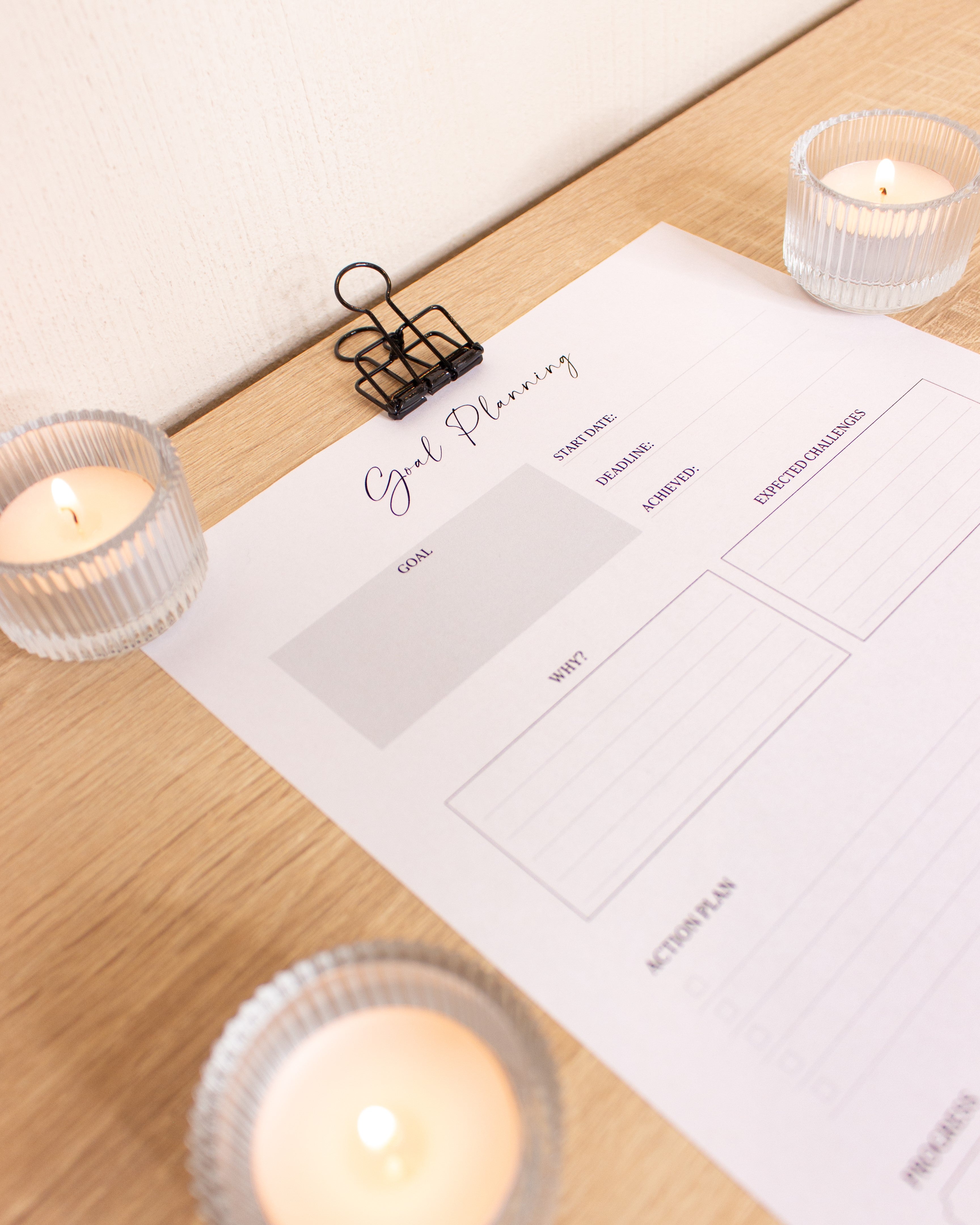 Sheet of paper with a goal planning template on light wood with a beige wall and candles in the background.
