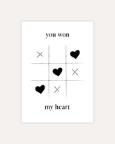 A postcard design showing a game of tic-tac-toe being won with heart symbols. Text saying "you won my heart" is split up with the first two words being above the game and the rest below it. The design is shown on a beige background.